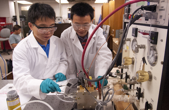 Research associates Yongjun Leng, left, and Nanwen Li place a membrane electrode assembly into the fuel cell stand for data analysis in their Reber Building laboratory.